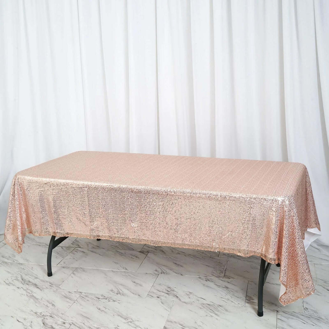 Rose gold sequin tablecloth on a table against a white backdrop.