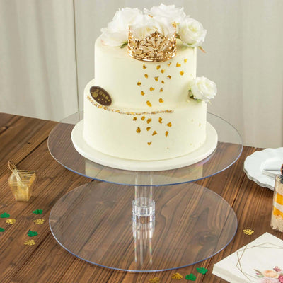 Elegant two-tier cake with gold crown and flowers on a clear cake stand.