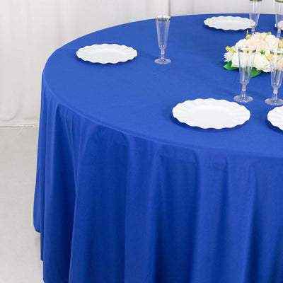 Blue tablecloth draped over a round table set with white plates and floral centerpiece.