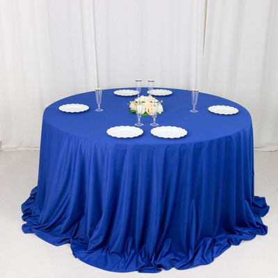Round blue tablecloth draped elegantly on a table with white plates and floral centerpiece.