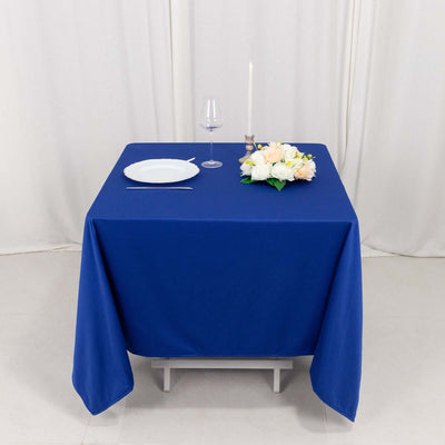 Blue tablecloth set with a plate, glass, candle, and flowers on a table.