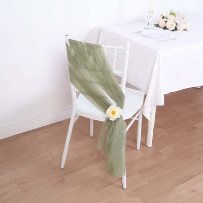 Olive green chair sash with flower decoration on a white chair in a dining setting.