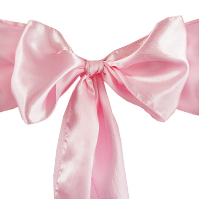 Pink satin bow with long tails on a plain background.