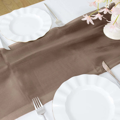 Brown table runner on a dining table set with white plates and floral decor.