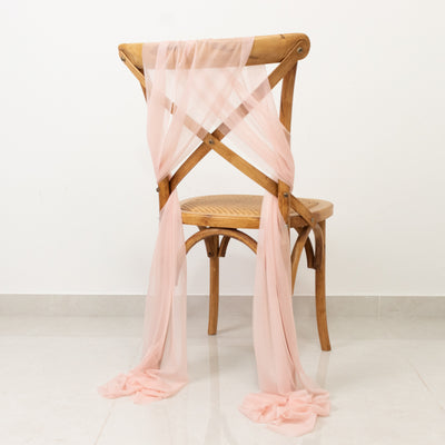Wooden chair draped with pink tulle fabric on a plain background.
