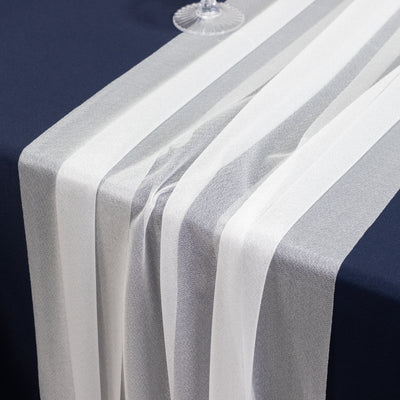 White and silver sheer table runner draped on a dark blue table.