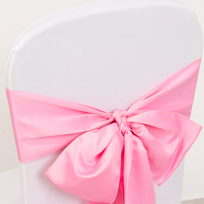 Pink satin chair sash tied in a bow on a white chair.