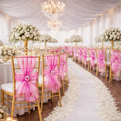 Elegant wedding reception setup with gold chairs and pink sashes, adorned with floral centerpieces.
