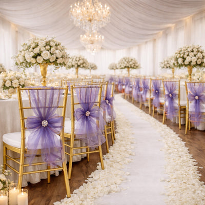 Elegant wedding reception setup with gold chairs and purple sashes, floral centerpieces.