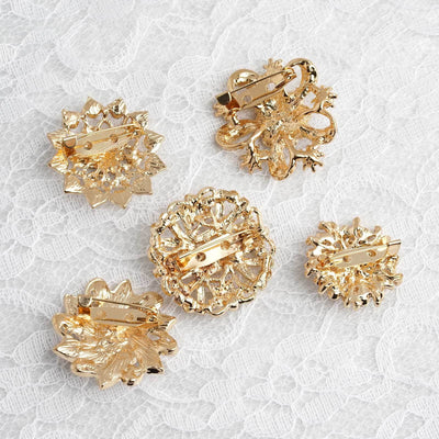 Five elegant gold floral brooches on lace background.