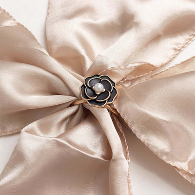 Black and gold flower ring with a pearl center on a satin ribbon.