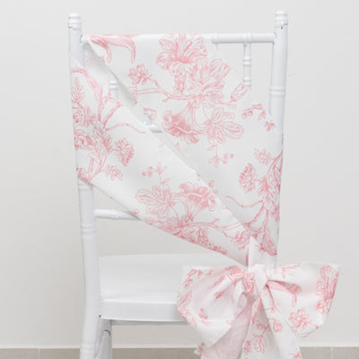 Pink floral patterned chair sash draped on a white chair.