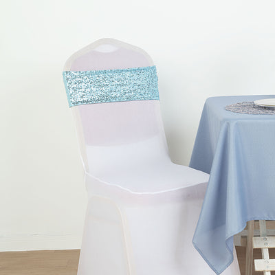 White chair cover with blue sequin sash on a table setting.