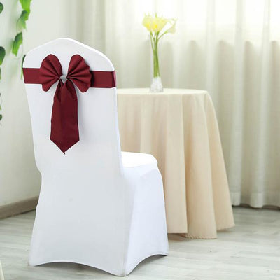Elegant white chair cover with burgundy bow in a styled interior setting.