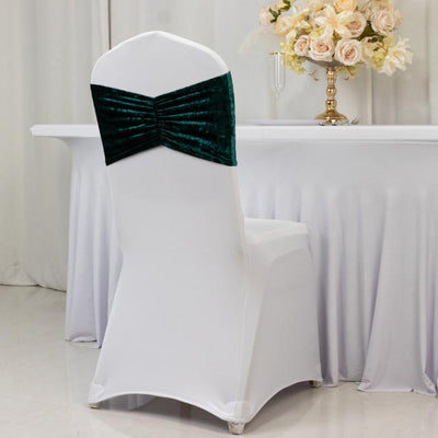 Elegant white chair cover with green velvet bow at a stylish event table.
