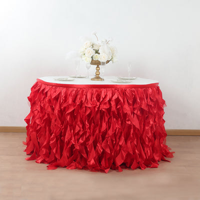 Red ruffled table skirt draping over a white table with floral centerpiece.