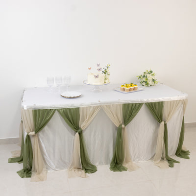 Decorated table with cake and desserts, draped in green and beige fabric.