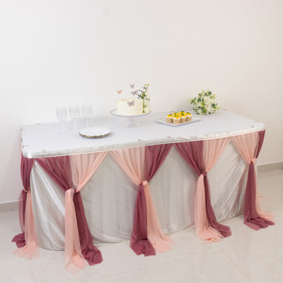 Decorated table with cake and flowers, draped in pink and burgundy fabric.