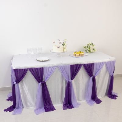 Decorated table with purple drapes, cake, and floral arrangements.