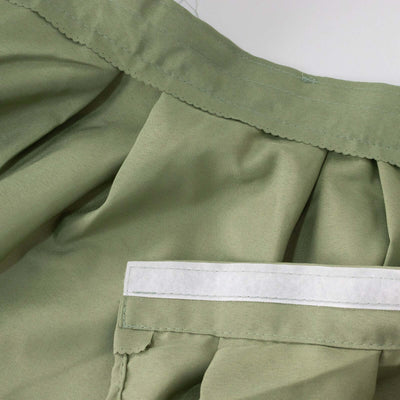 Green pleated fabric with a white label attached, studio shot.