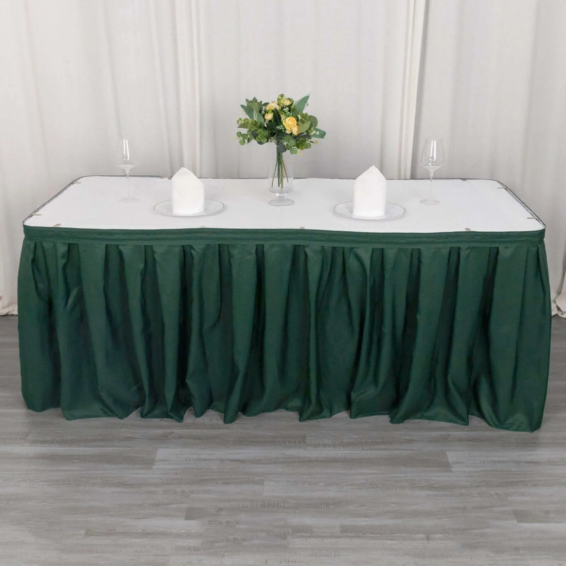 Green table skirt draped over a table set with plates and a vase of flowers.