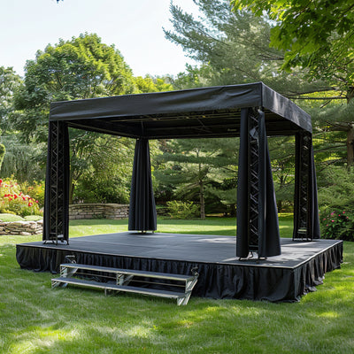 Outdoor black stage with curtains and steps in a garden setting.