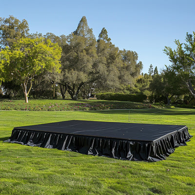 Black stage platform with draped skirt in a green outdoor setting.