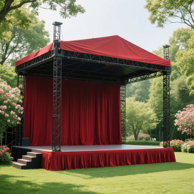 Outdoor event stage with red drapes and canopy, surrounded by greenery.