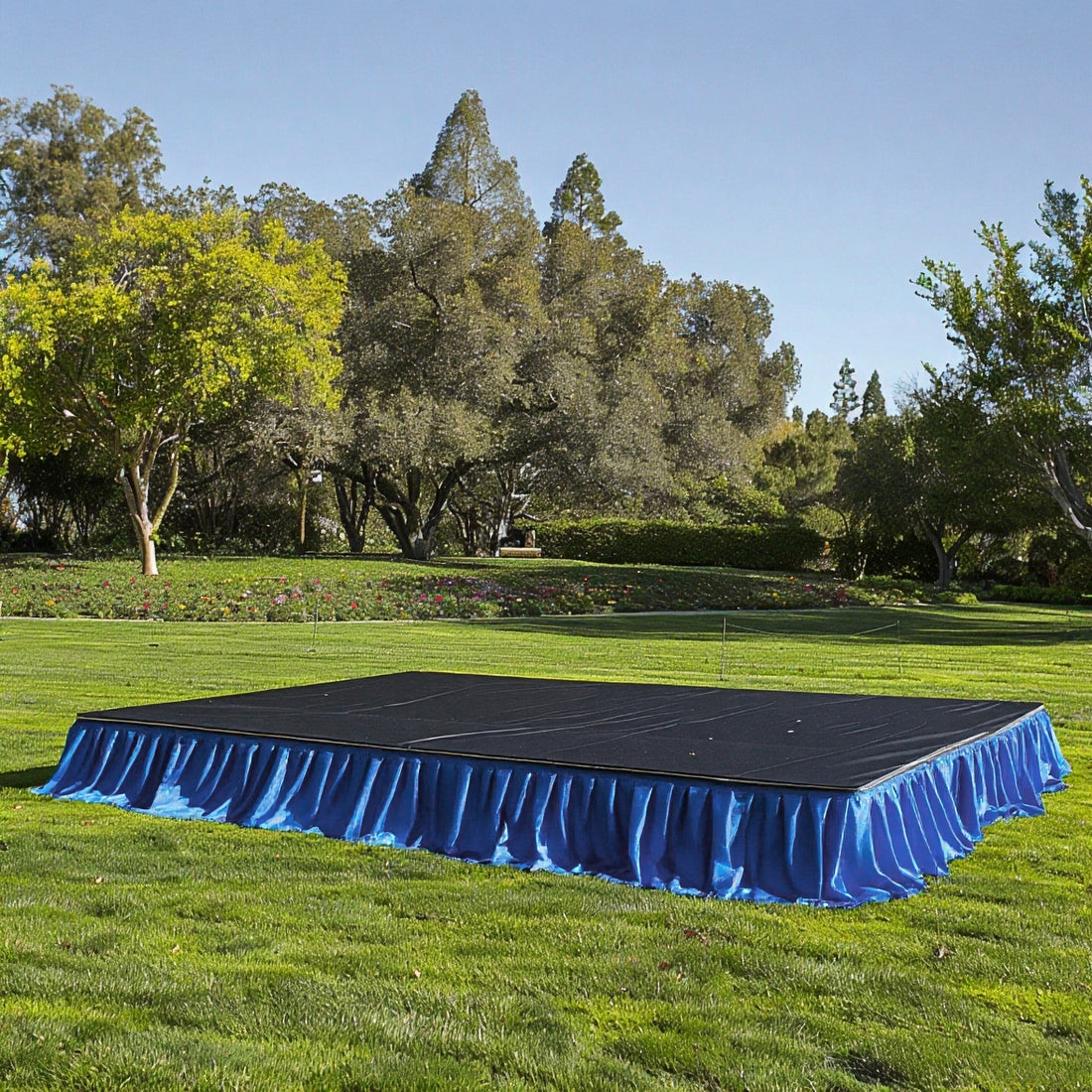 Outdoor event stage with blue skirting in a grassy park setting.