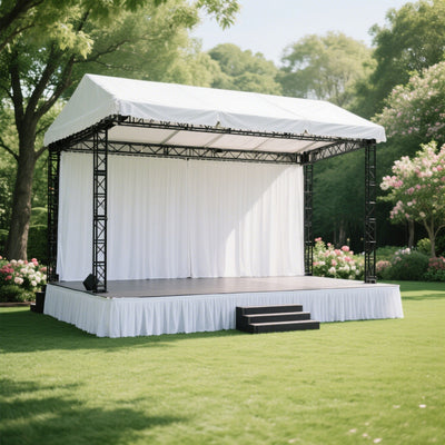 Outdoor event stage with white drapes and black frame in a garden setting.