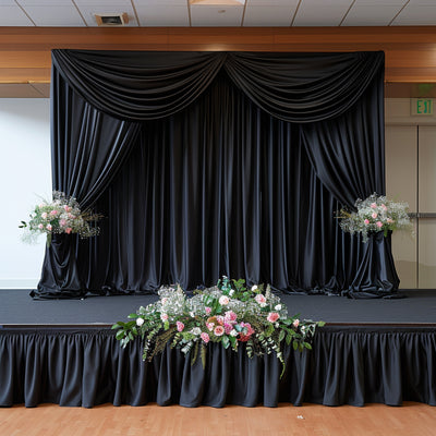Black stage curtain with floral arrangements at the base.