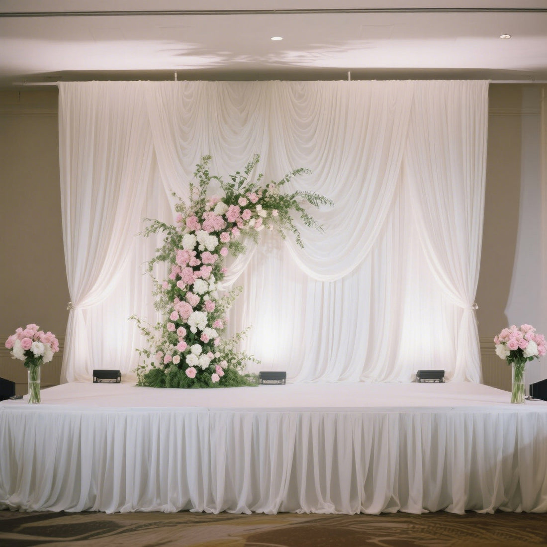 Elegant wedding stage setup with draped white fabric and floral arrangements.