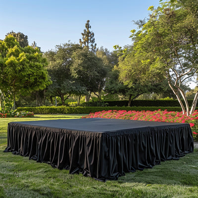 Outdoor event stage with black skirting in a garden setting.