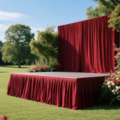 Outdoor red stage with curtains in a lush garden setting.
