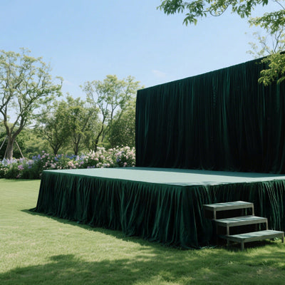 Outdoor stage with green velvet curtains and steps in a garden setting.