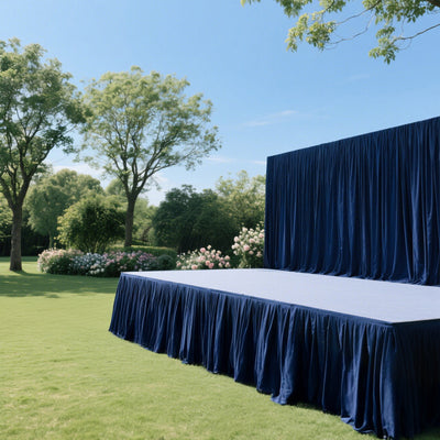 Outdoor event stage with blue drapes and lush greenery in the background.