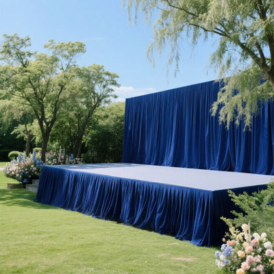 Outdoor stage with blue drapery and lush greenery backdrop.