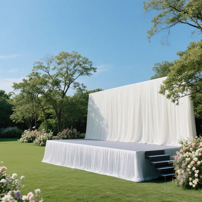 Outdoor event stage with white drapery and lush greenery.