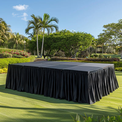 Outdoor event stage with black skirt in a lush garden setting.