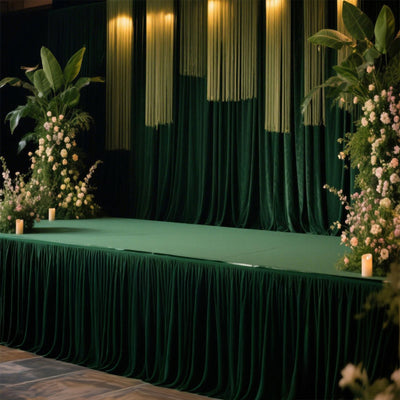 Elegant event stage with green drapery and floral arrangements.