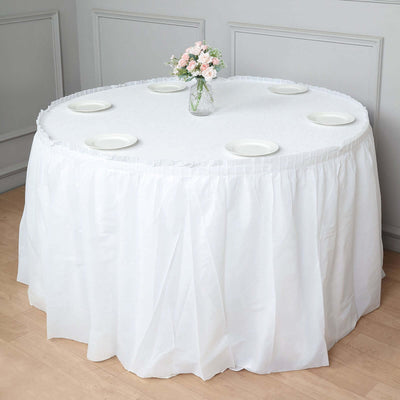 Round table with white tablecloth, plates, and flower vase.