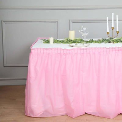 Pink table skirt draped over a table with candles and greenery decoration.
