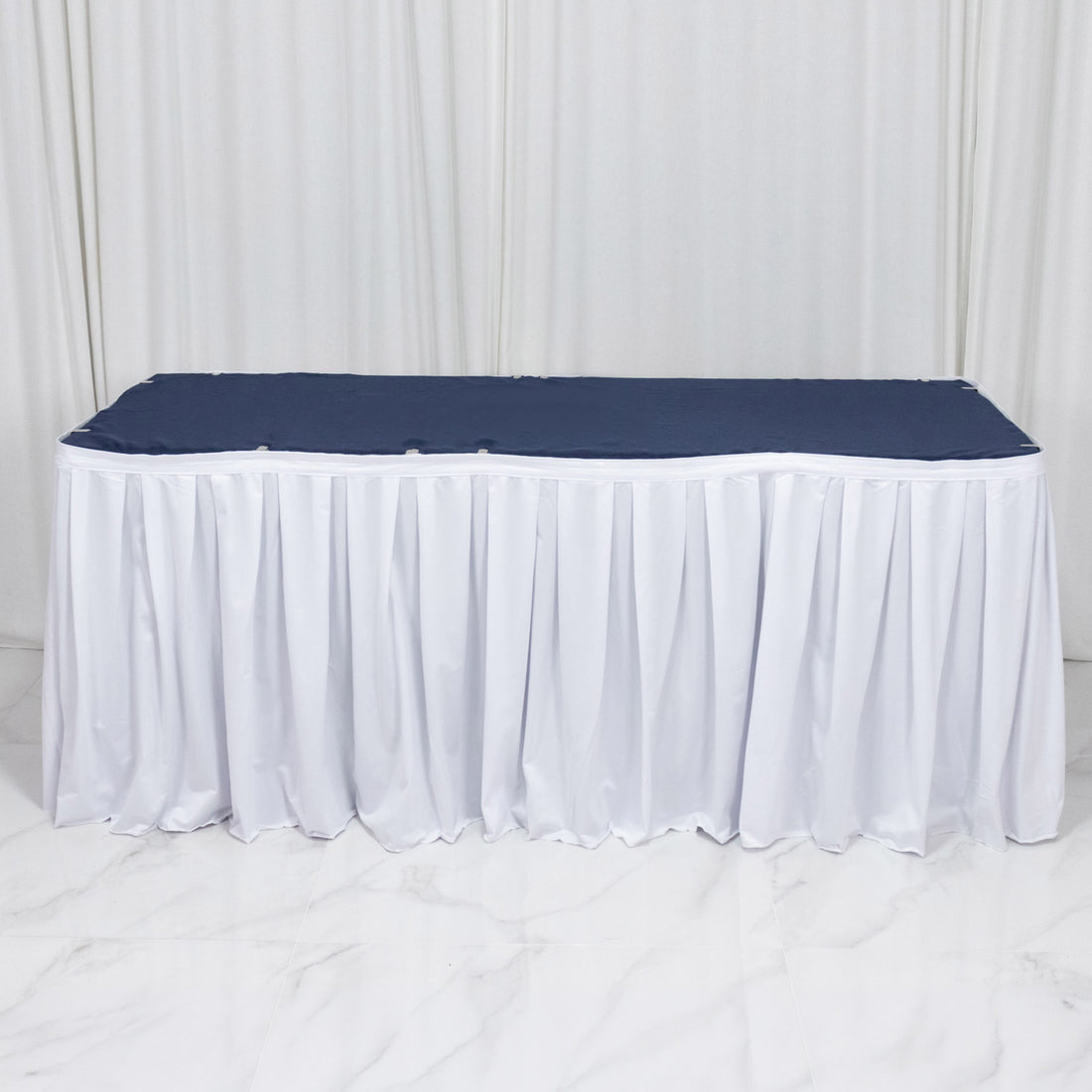 White banquet table with navy table cover and white pleated skirt on display