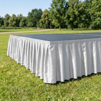 White pleated stage skirt on outdoor event platform in park