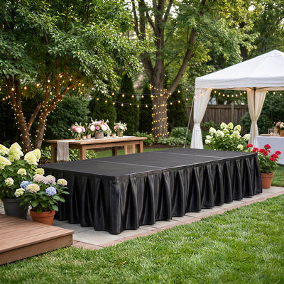 Outdoor event stage with black skirt, floral decor, string lights, and white tent