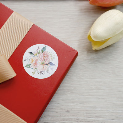 Red gift box with floral sticker and ribbon on wooden surface.