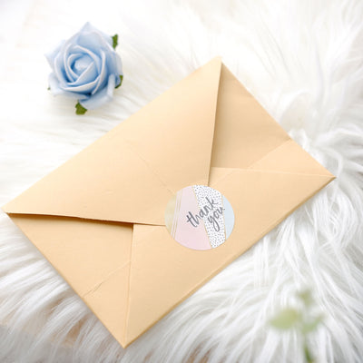 Thank you card in envelope with decorative sticker on soft, textured background.