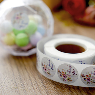 Thank You sticker roll with floral design and pastel candy balls in a clear container.