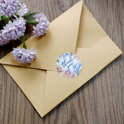 Yellow envelope with floral "thank you" sticker and pink flowers nearby.