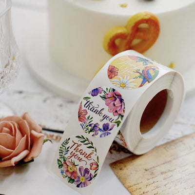 Floral "Thank You" sticker roll on a table with cake and decorations.